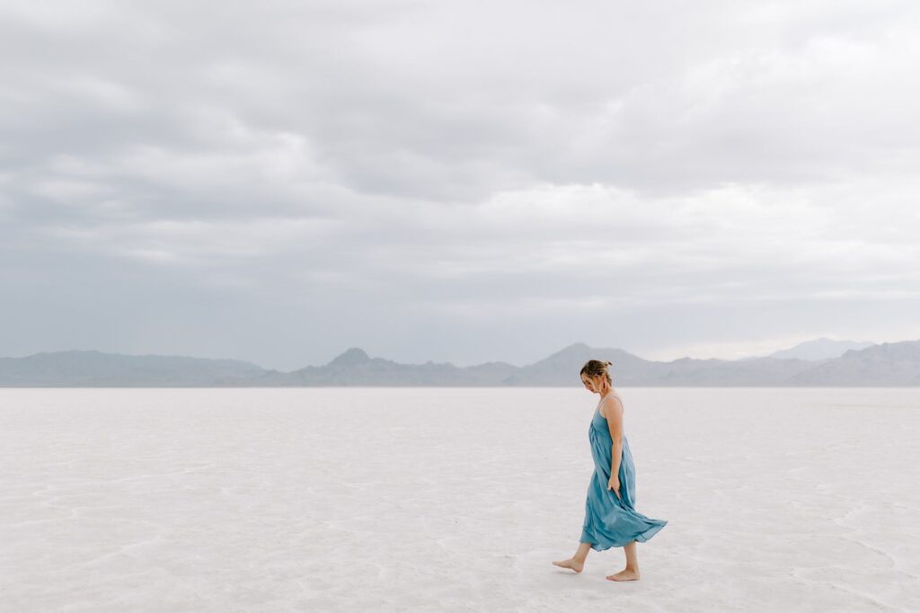 a woman in blue dress walking on white sand