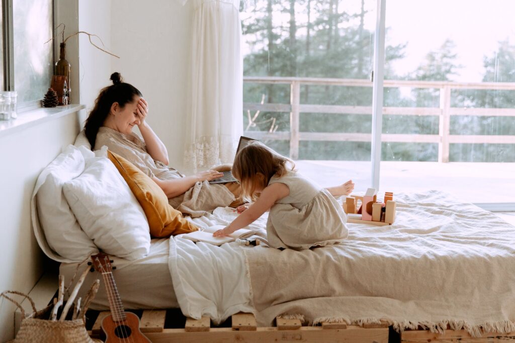 laughing mother working and playing with daughter on bed at home