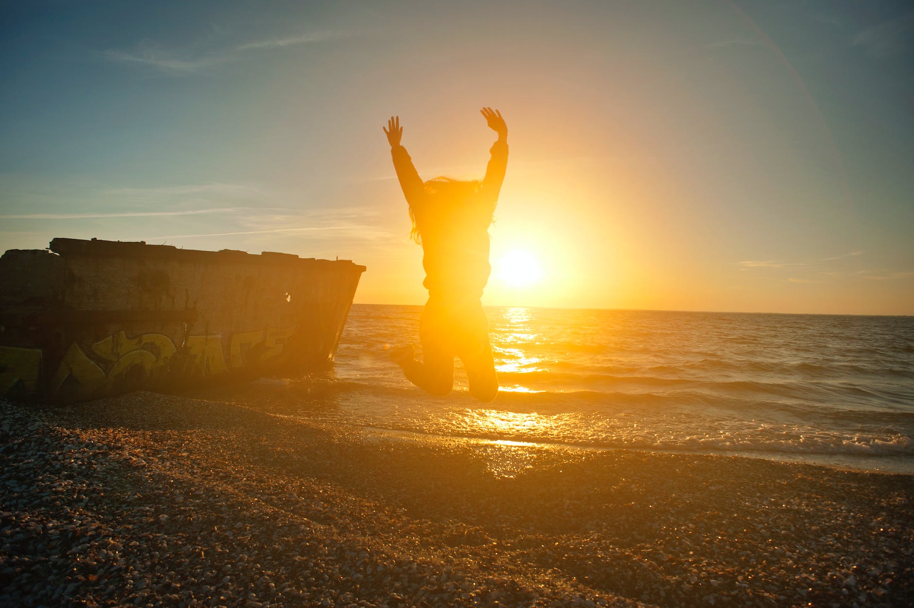 person jumping on seashore during golden hour