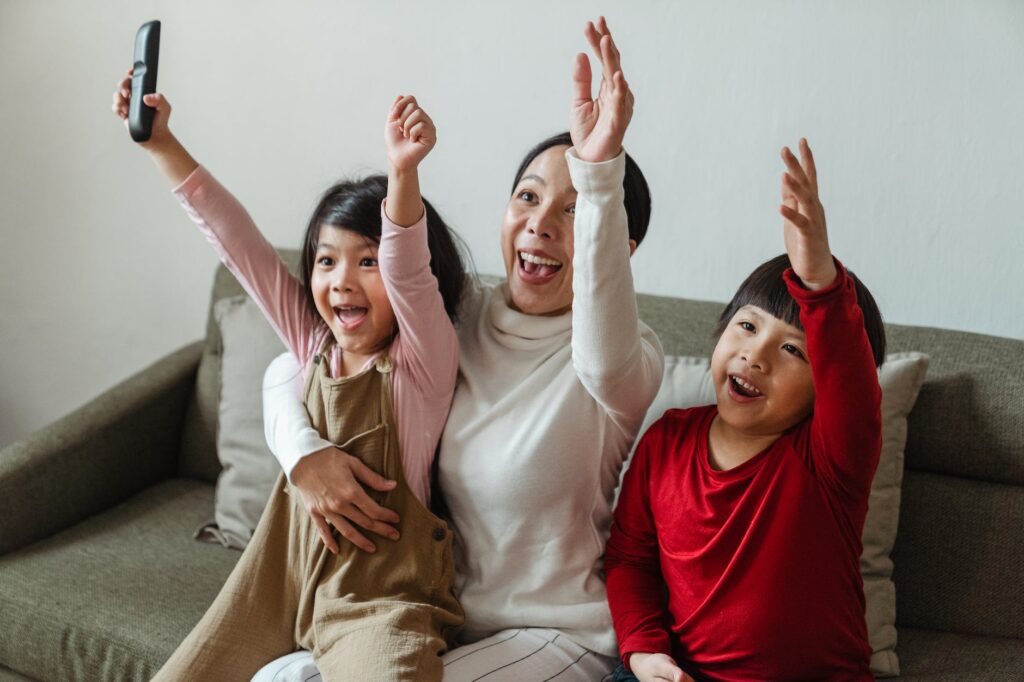 positive ethnic mother with children watching football on tv and celebrating goal